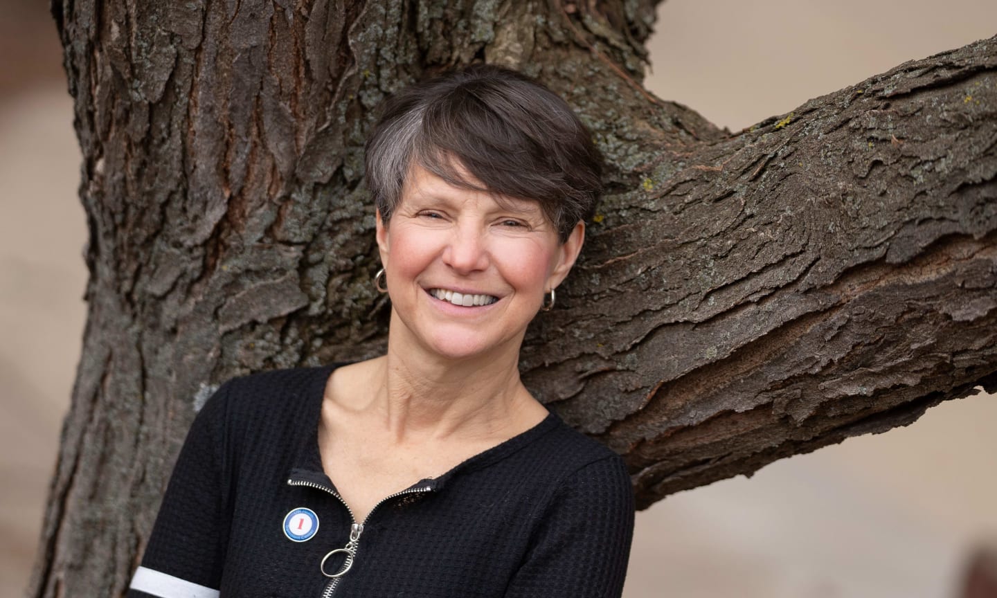 Woman leaning against a tree and smiling.