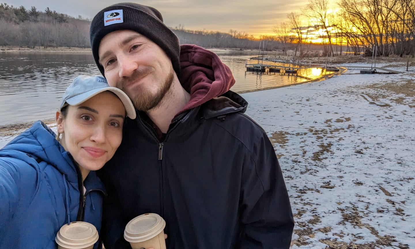 Woman smiling next to man, both holding coffees and standing outdoors on a snowy day.