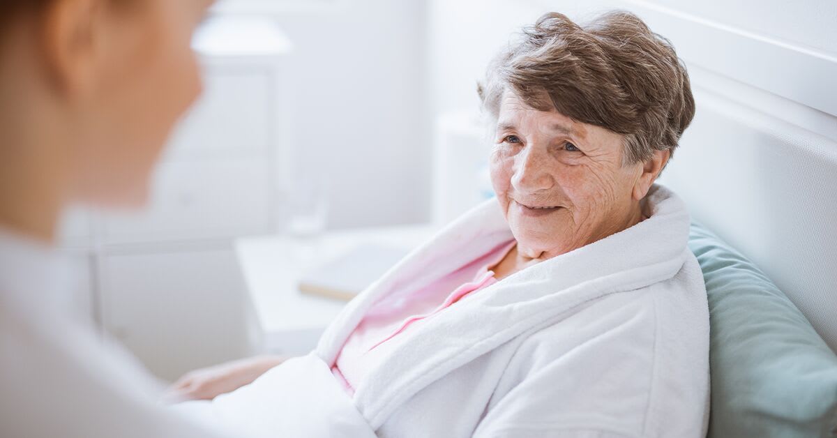 An older woman lying in bed next to a caregiver
