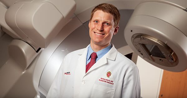 A cancer doctor standing in front of a radiation therapy machine