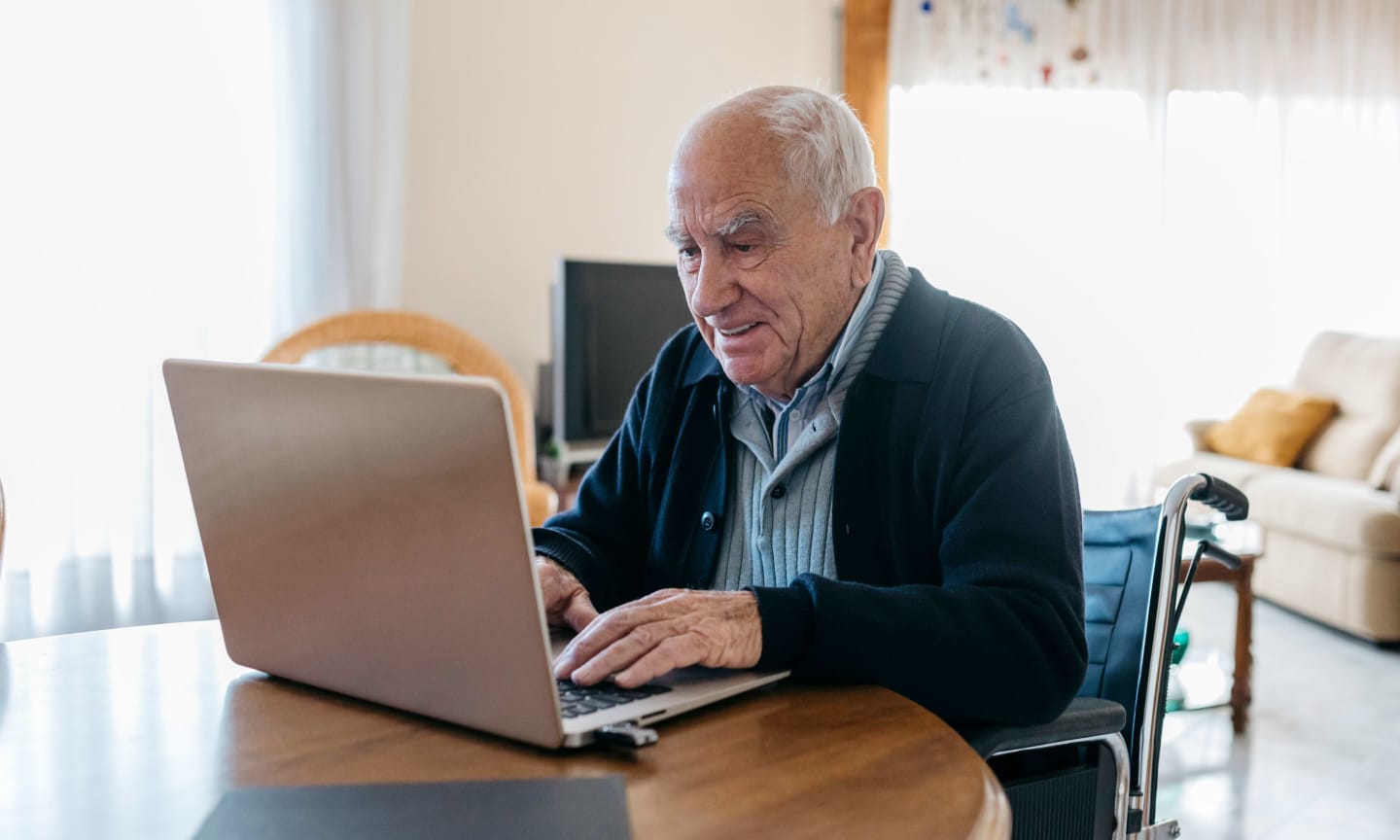 Older individual in a wheelchair at a table working on a laptop