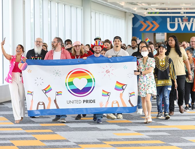 A large group of diverse team members holding a pride banner