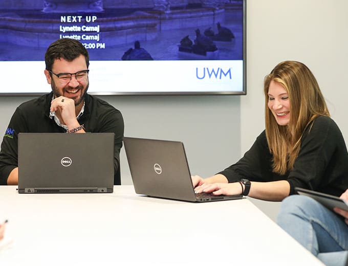 Two Risk Management team members smiling while on their laptops in a comference room