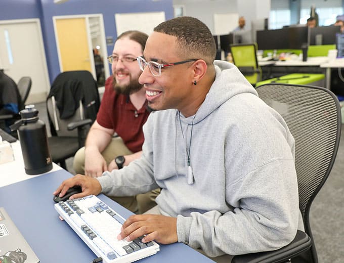 Two smiling Technology team members working together at a desk