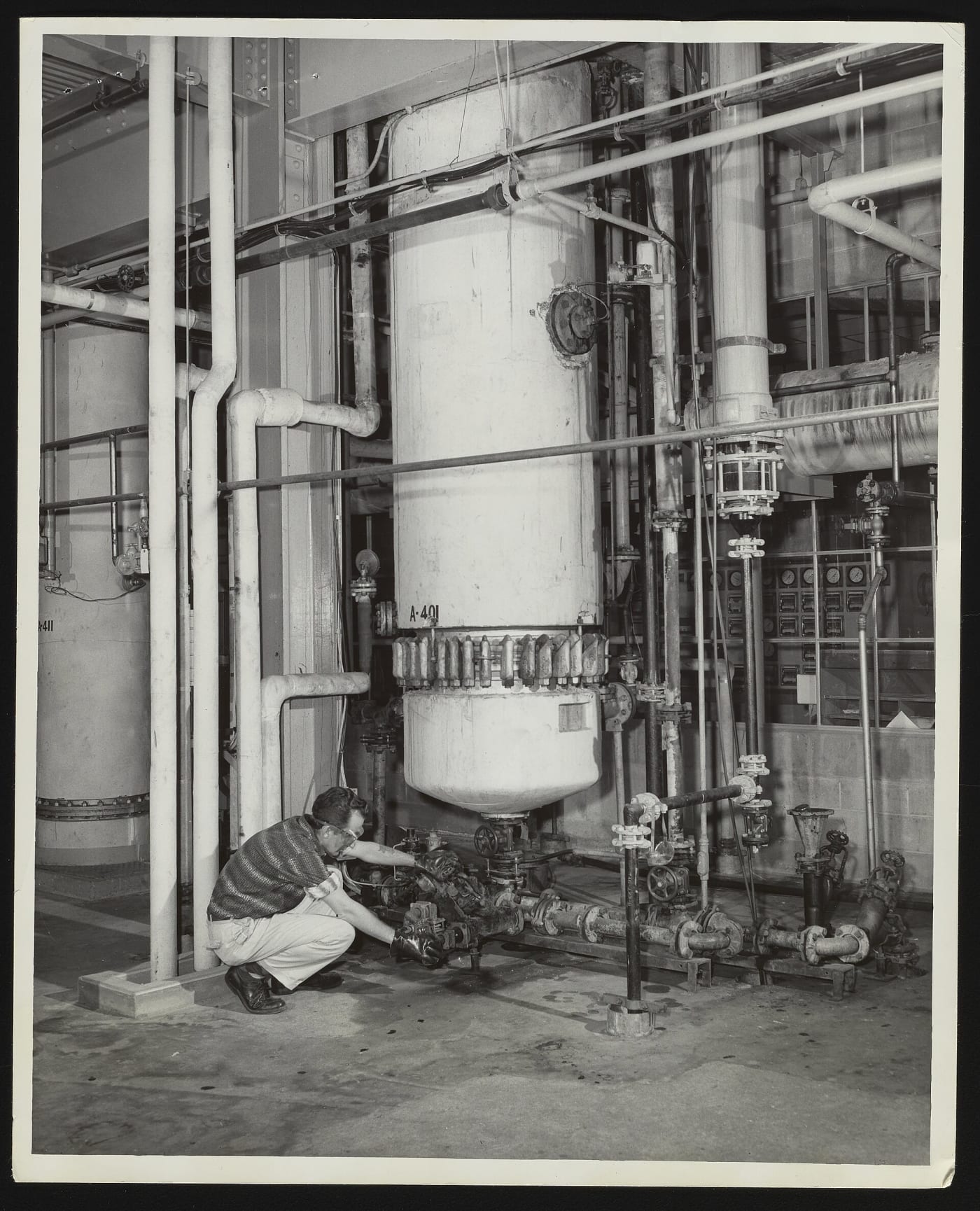 General view of an unidentified employee making an adjustment to the lower part of a hydrochlorinator unit at the Hercules Powder Company pl