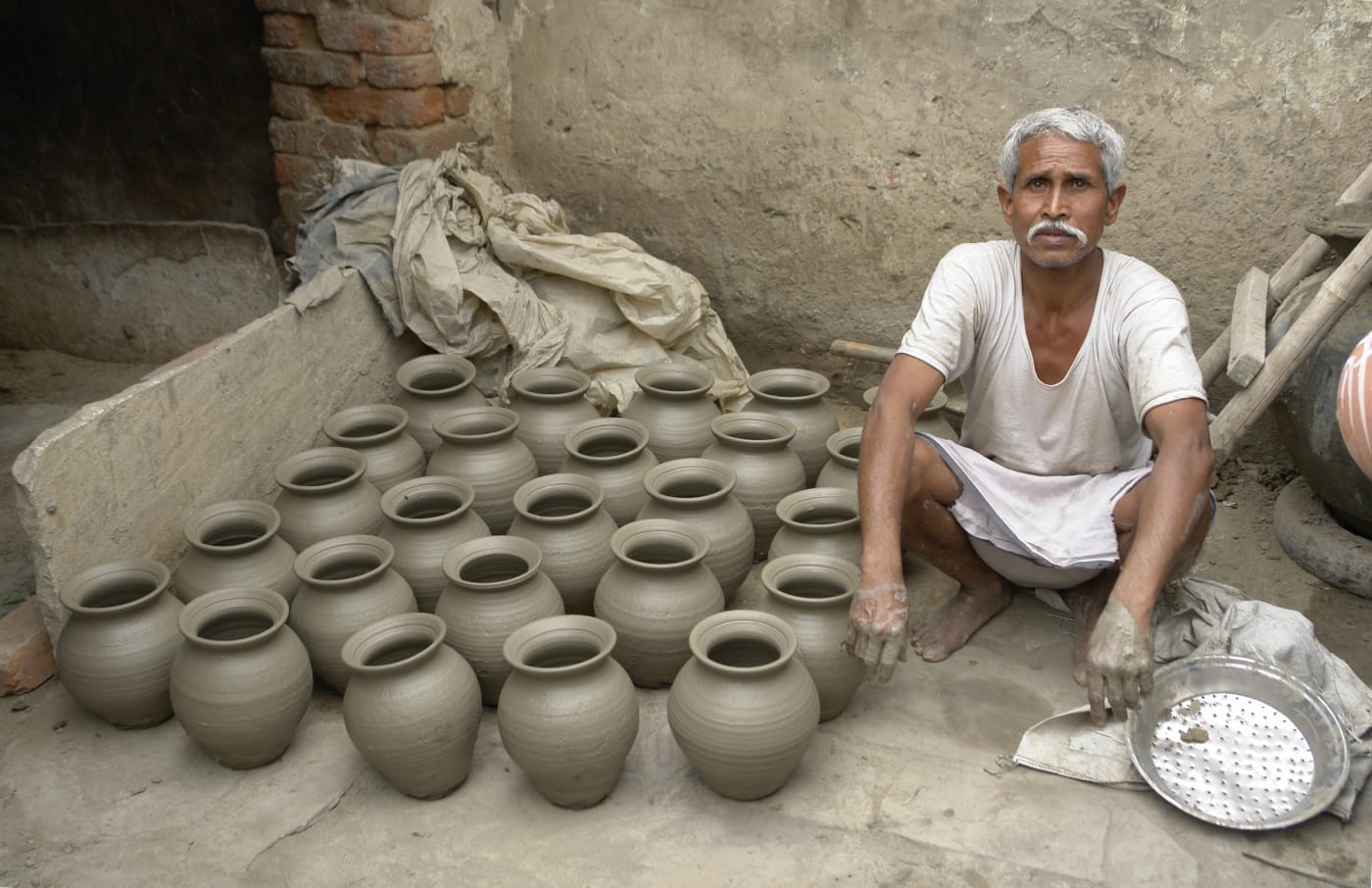 A potter at work with his day's rows of pots, Jaura.