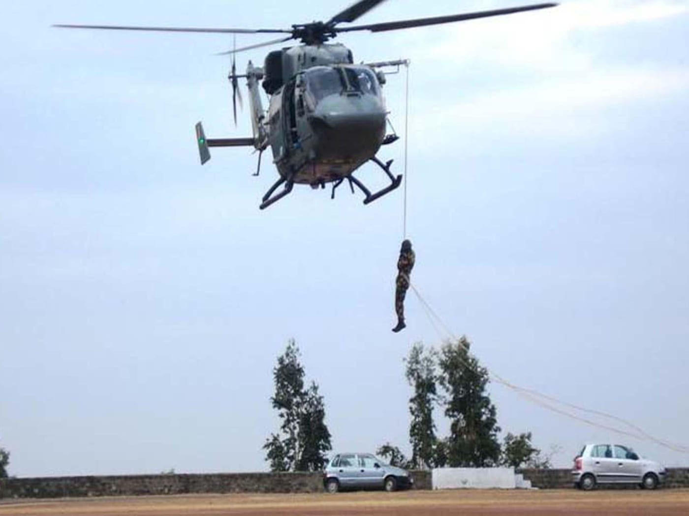An NDRF rescuer descending from a helicopter during training.