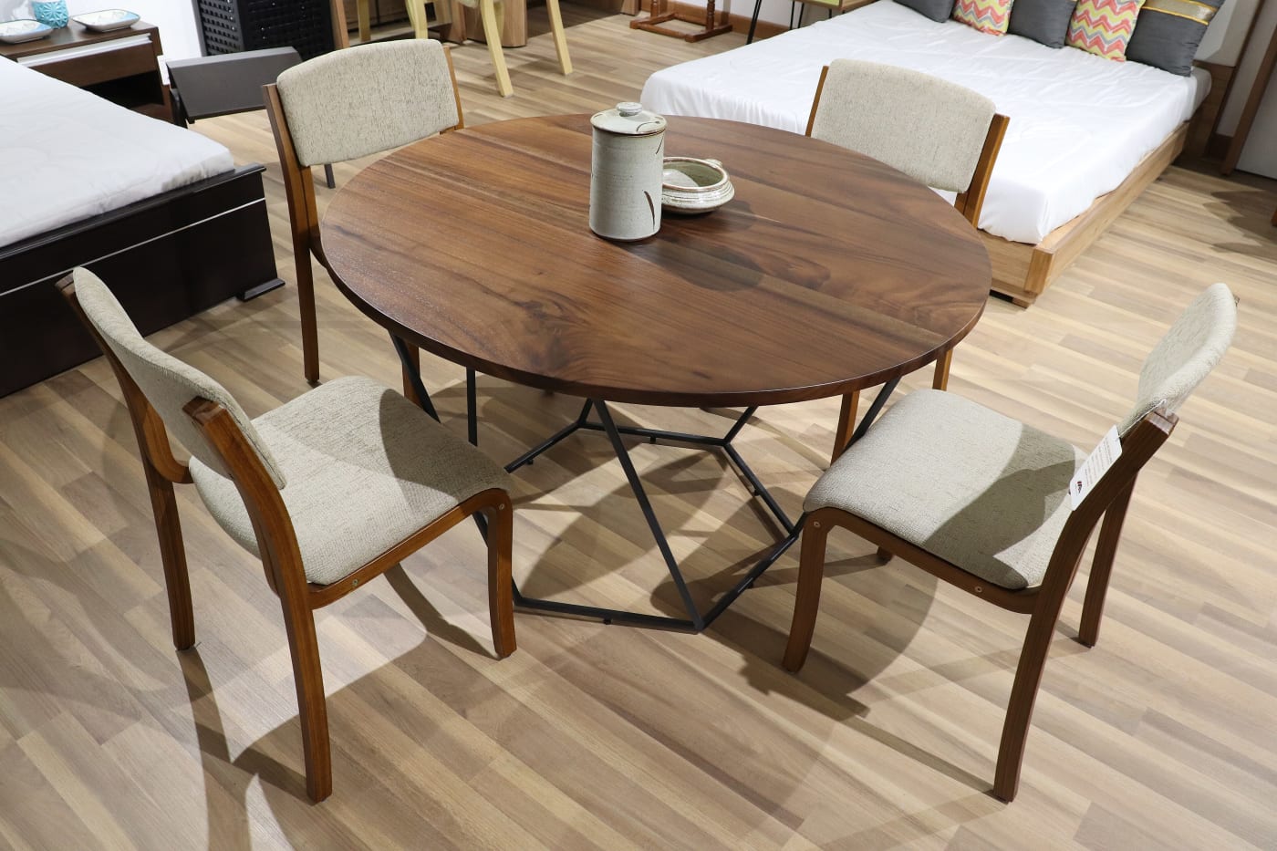 A round wooden dining table with four chairs on display in a furniture showroom in Hunsur, Karnataka.