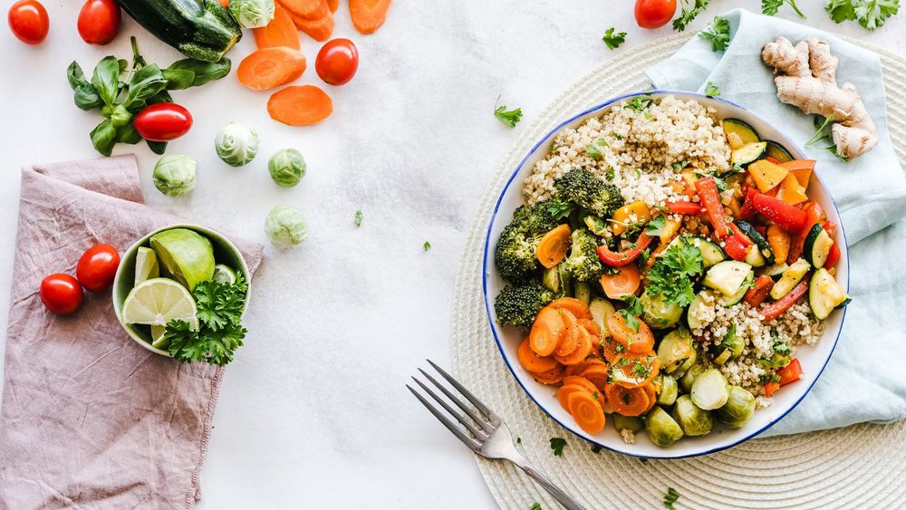 a round plate filled with different vegetables placed on a white cloth background with a fork on the side