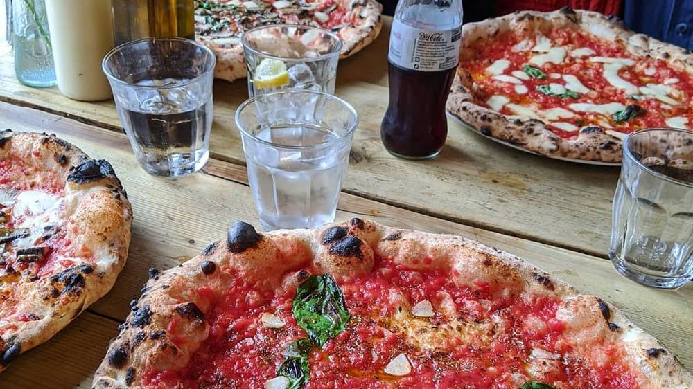 Four oven baked pizzaas kept on table with four glasses of water and a bottle of half filled soft grink.