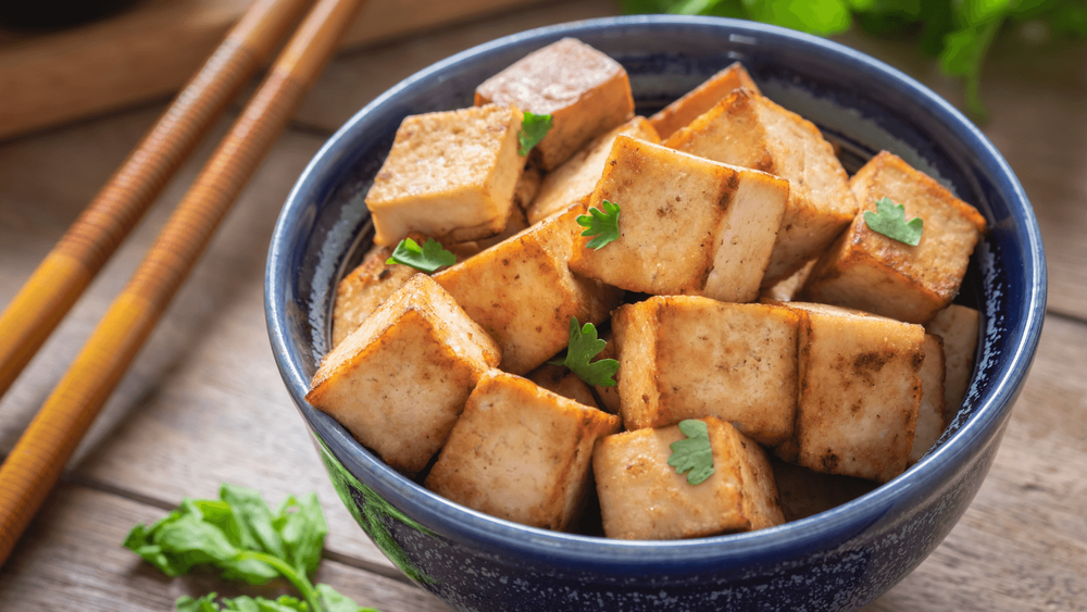 Pieces of tofu in a bowl on a table next to a pair of chopsticks