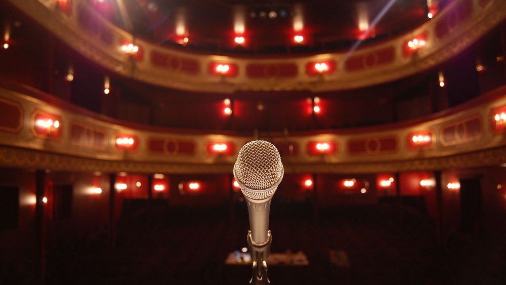  black and grey microphone on a stand, behind it is a theatre with multiple stands and red lights