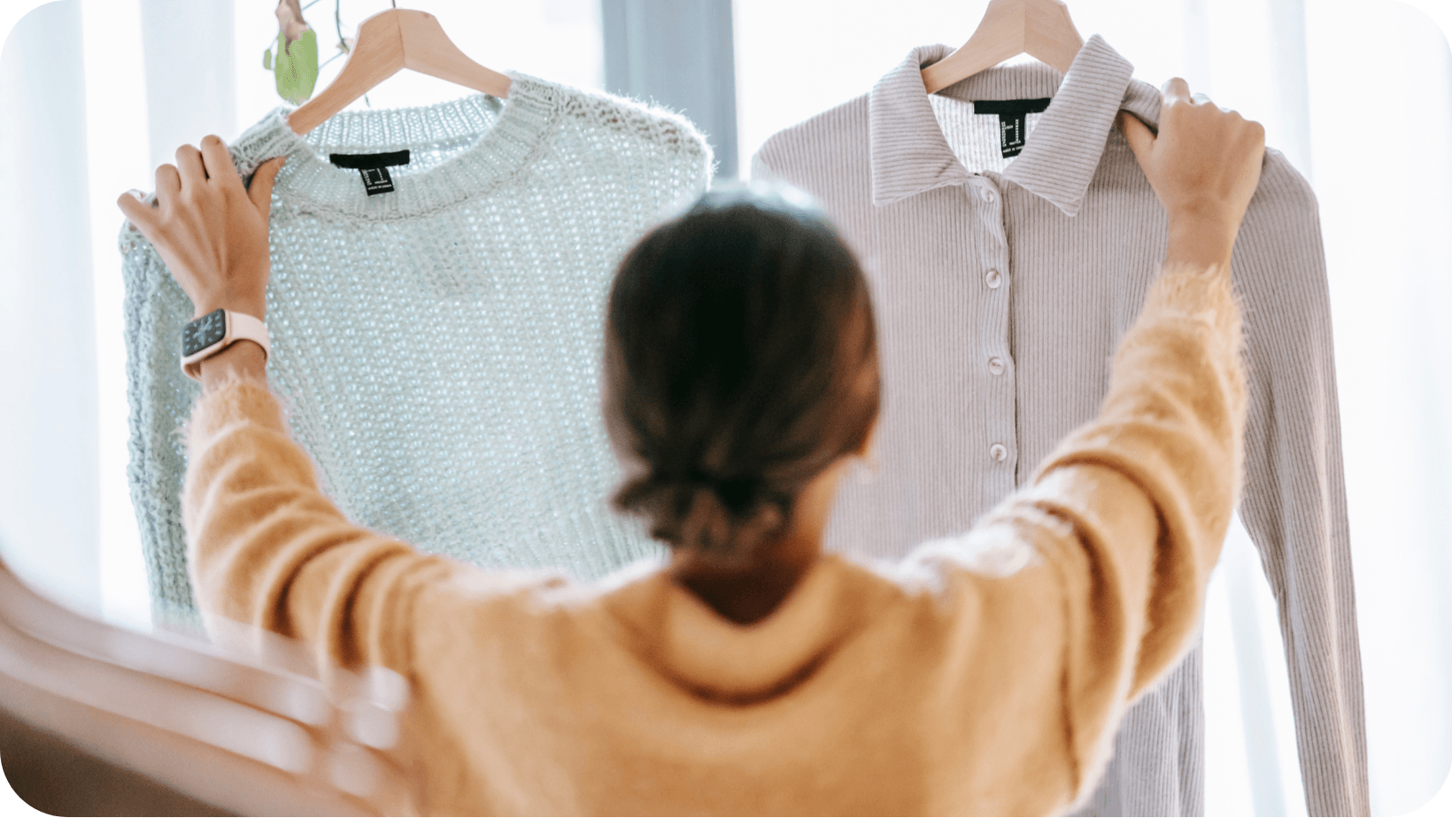 woman holding up a shirt and a jumper on hangers