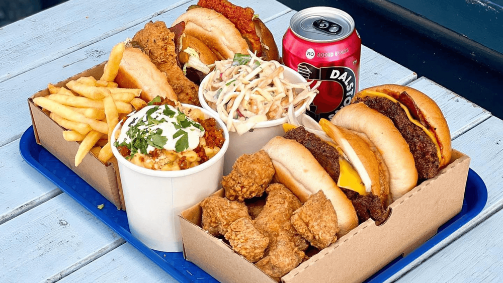 variety of burgers, chips, vegan meats, fizzy drinks on a blue tray on top of a white table