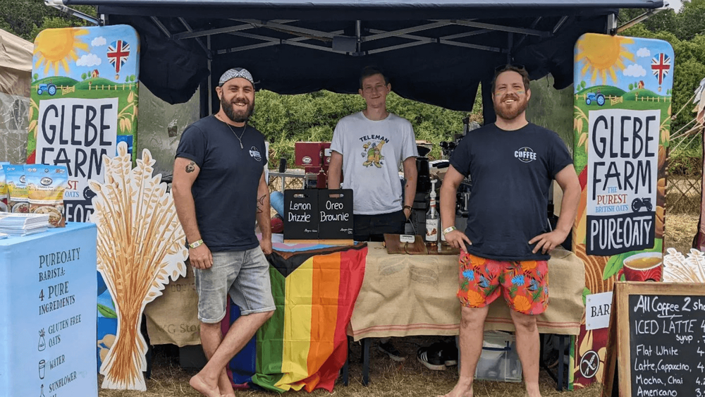 Three men in shorts standing next to an outdoor stall selling coffee and treats