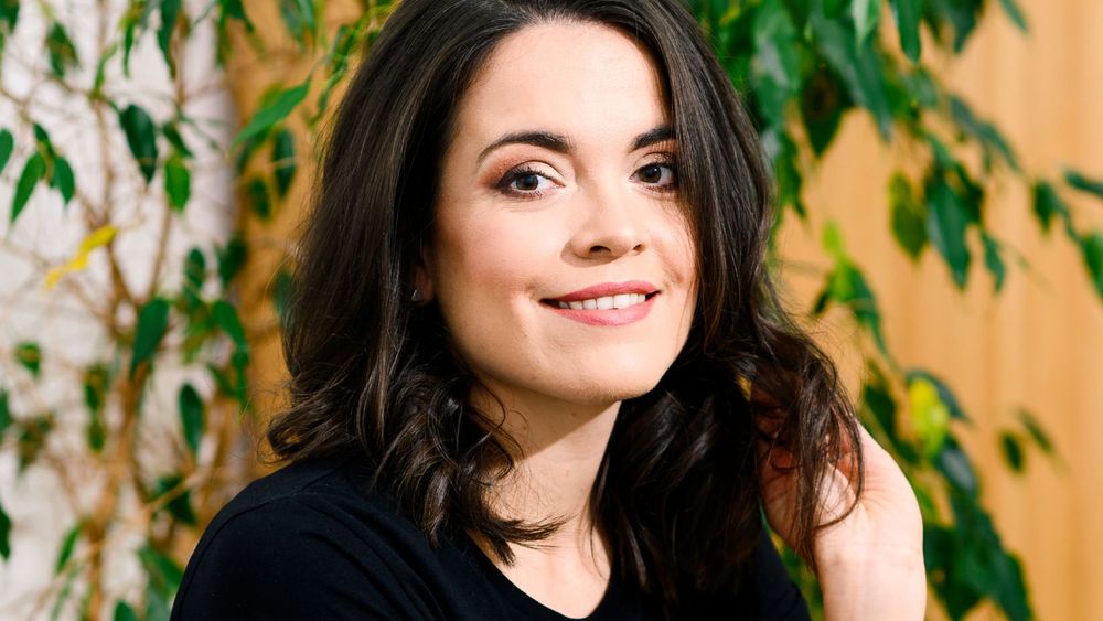 Photo of woman smiling (Sascha Camilli) in front of a green plant