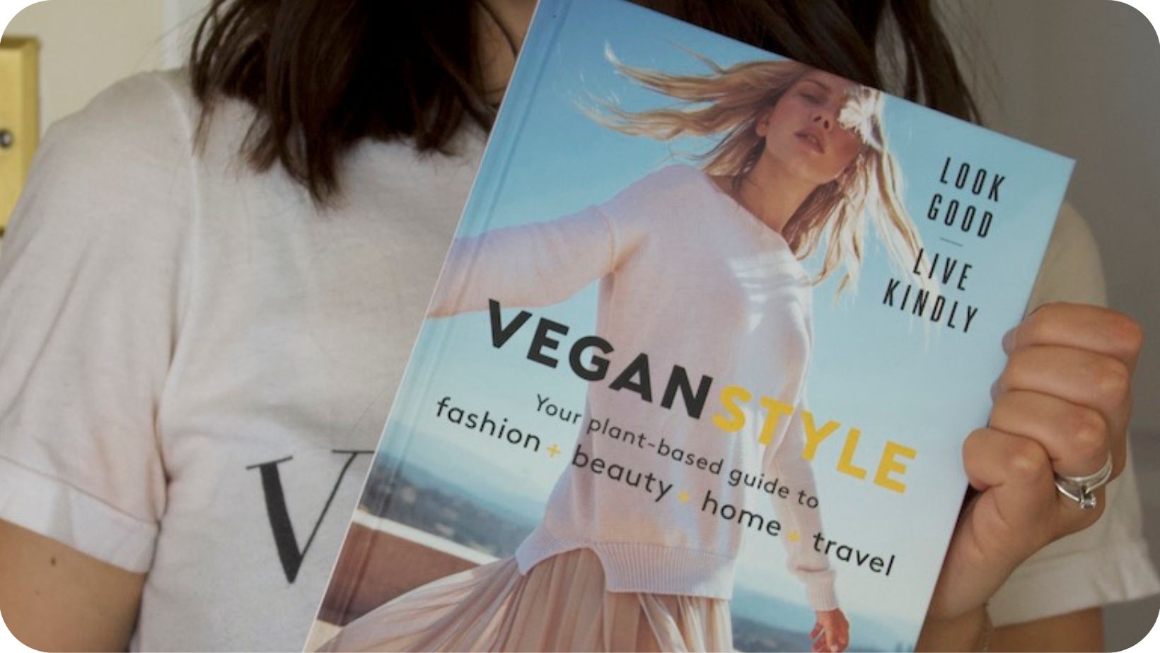 Woman (Sascha Camilli) holding  up her book Vegan Style in front of her