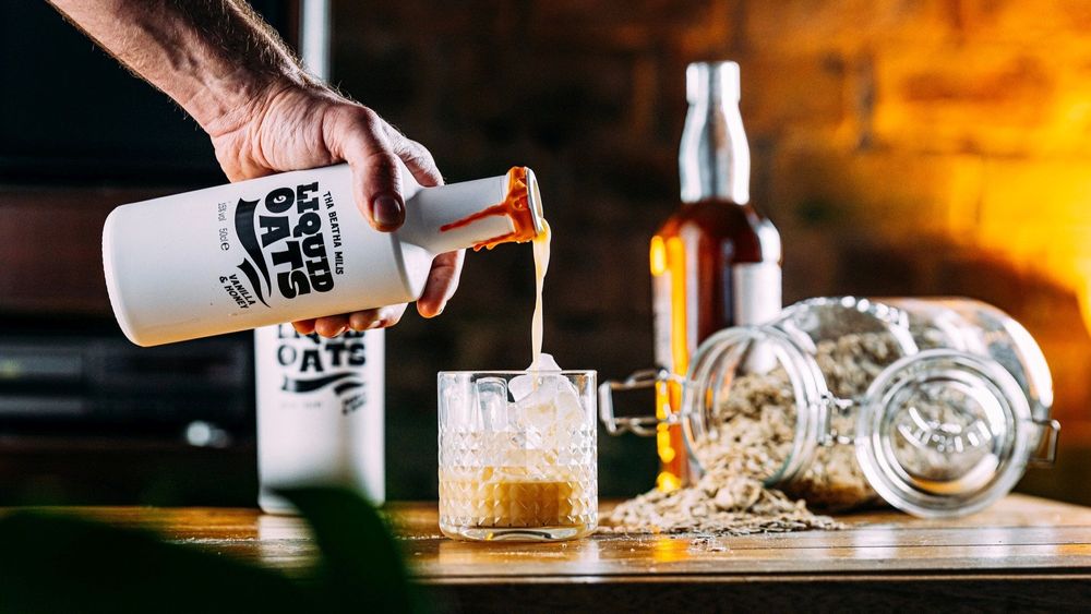 man pouring a bottle of Liquid Oats vegan cream liqueur into a glass full of ice