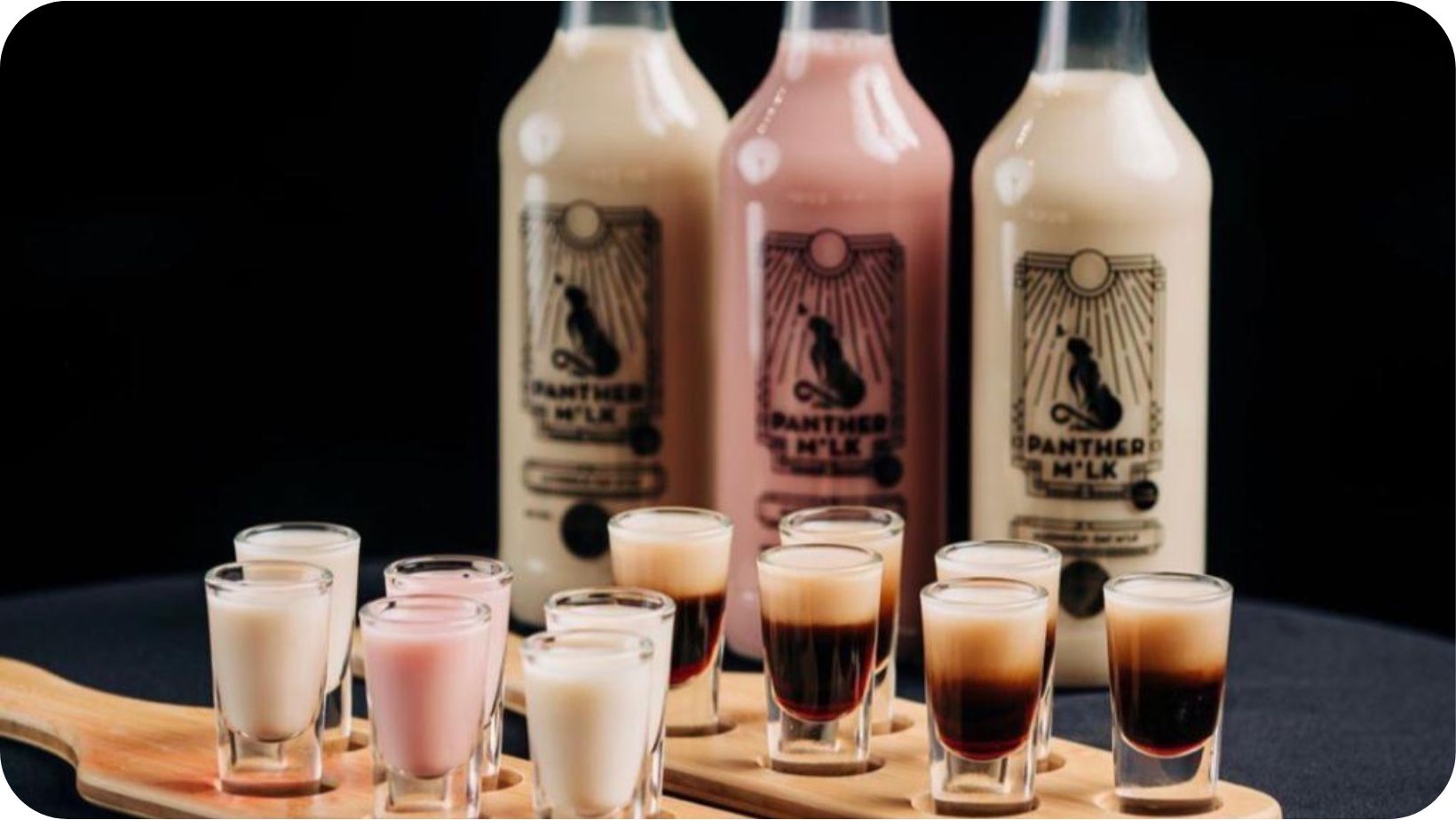 Different flavour bottles of Panther M*lk’s vegan cream liqueur with shot glasses full of the drink in front of them