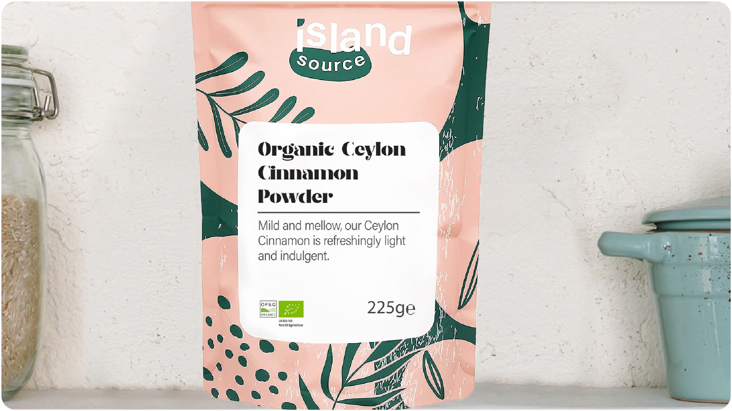 Pink and green pack of Island Source’s organic Ceylon cinnamon powder in front of white wall and cookware.