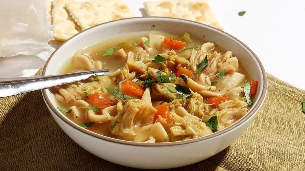 Jackfruit pieces in a soup in a soup bowl with a spoon in it and some crackers beside it 