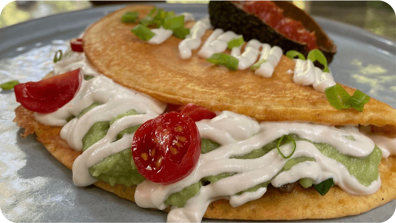 Vegan ‘omelette’ filled with avocado, tomato and mayo on a silver plate 