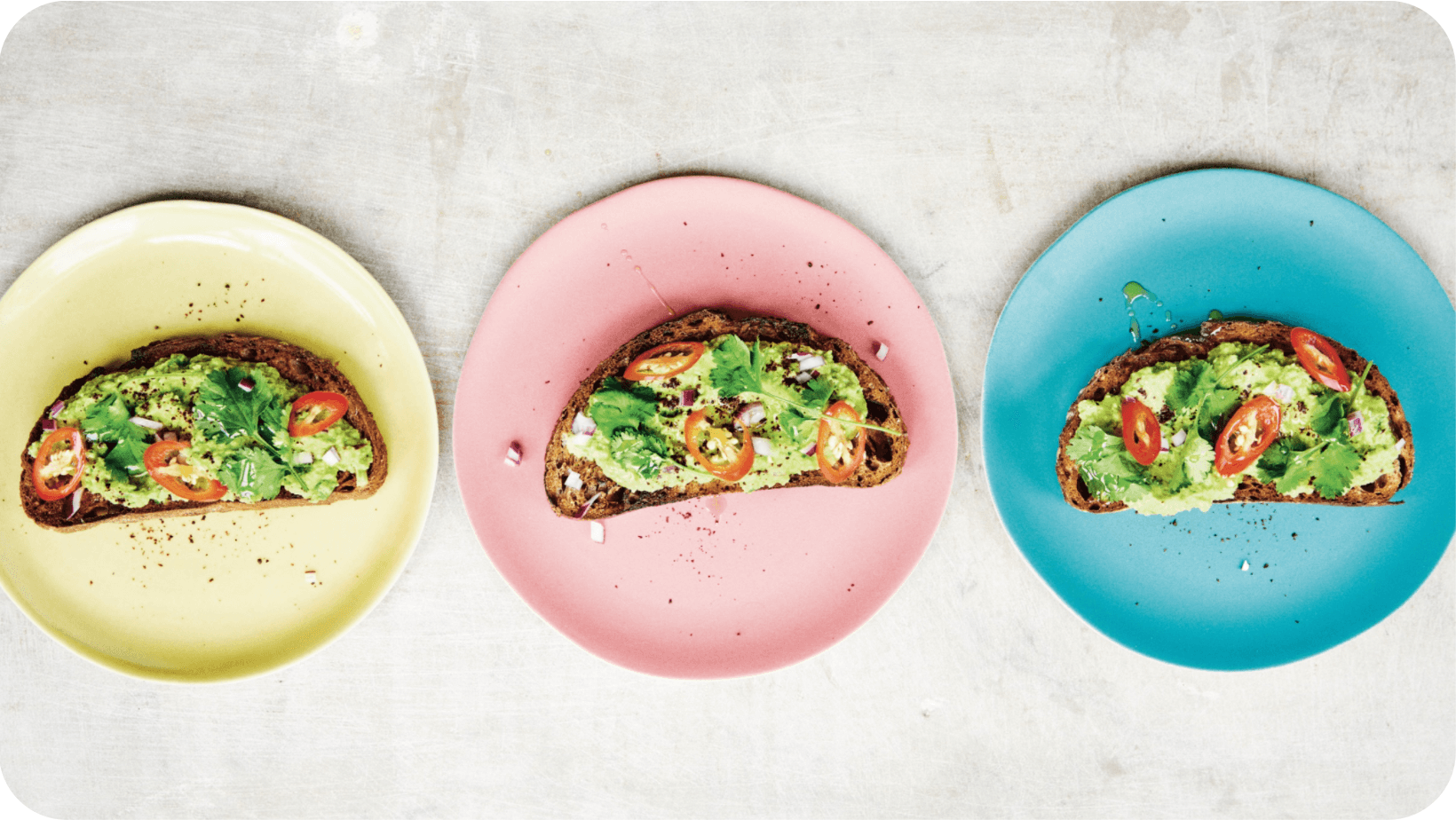 Three colourful plates with toast topped with avocado, tomato and coriander on each of them