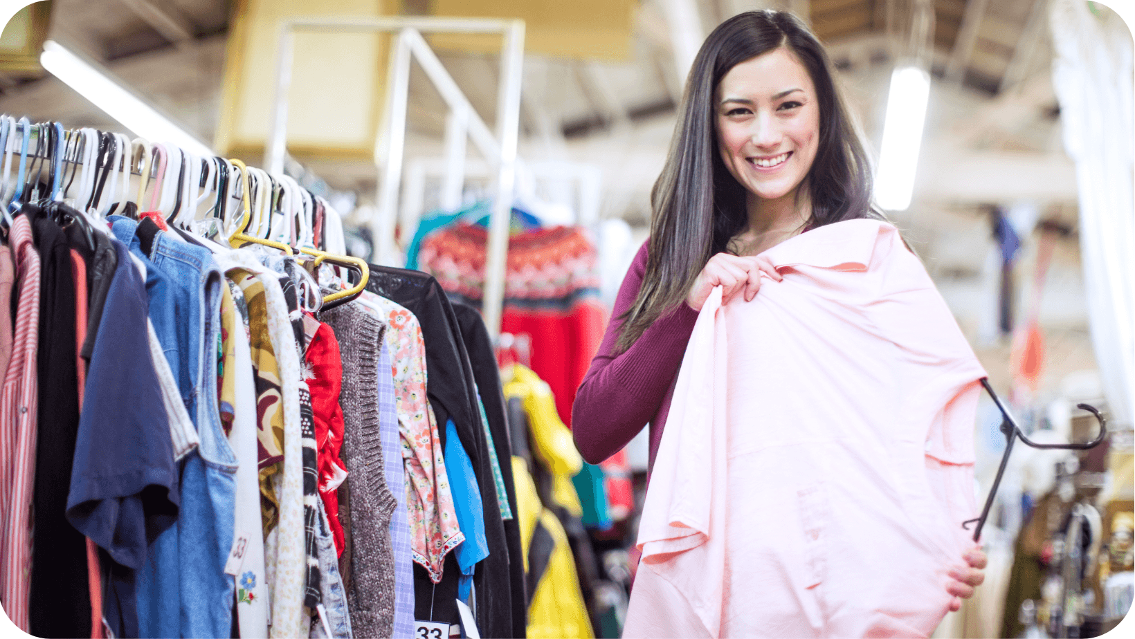 Smiling woman holding a pink top that she picked of a clothes rail in a second-hand clothes shop