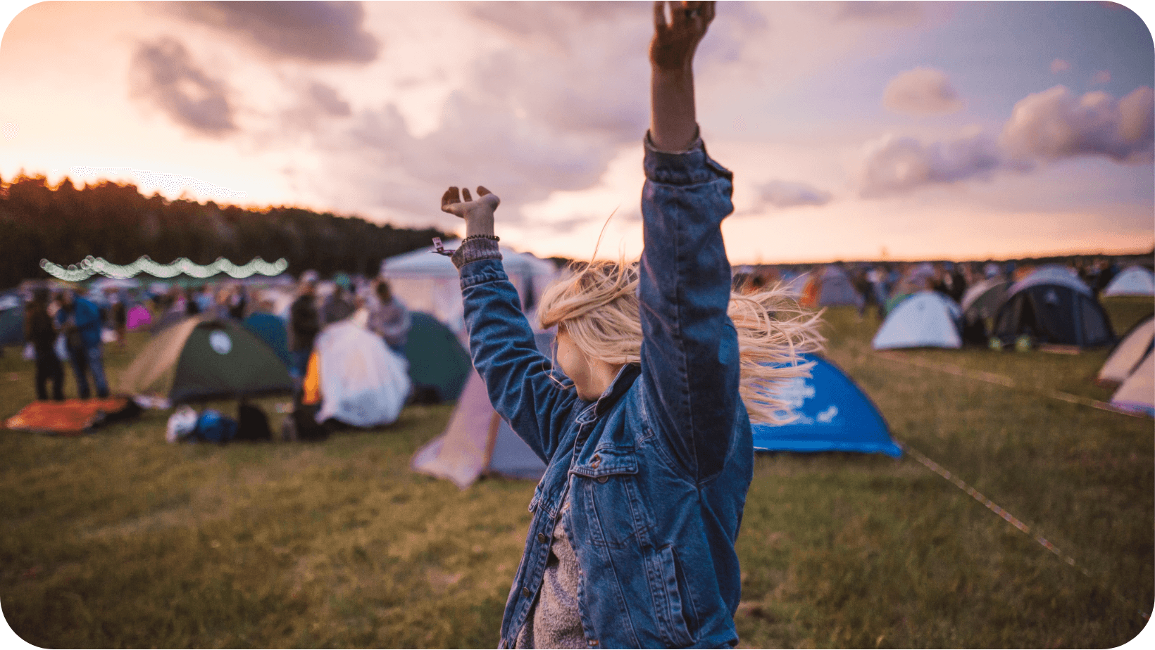  A woman raising her arms in front of tents at a music festival