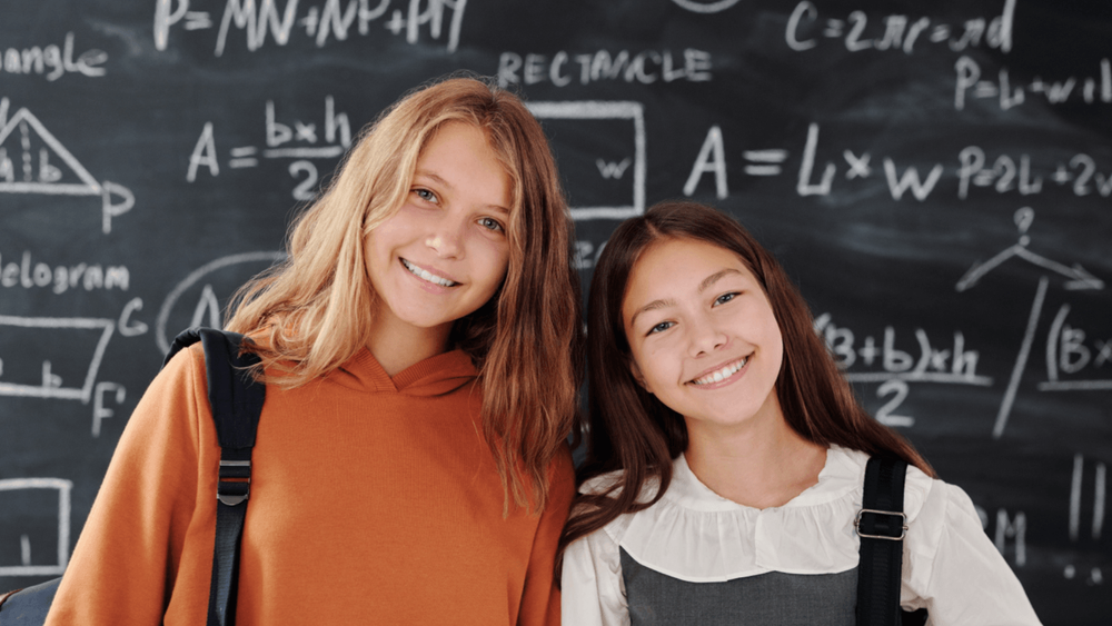 Two girls smiling in front of a blackboard 