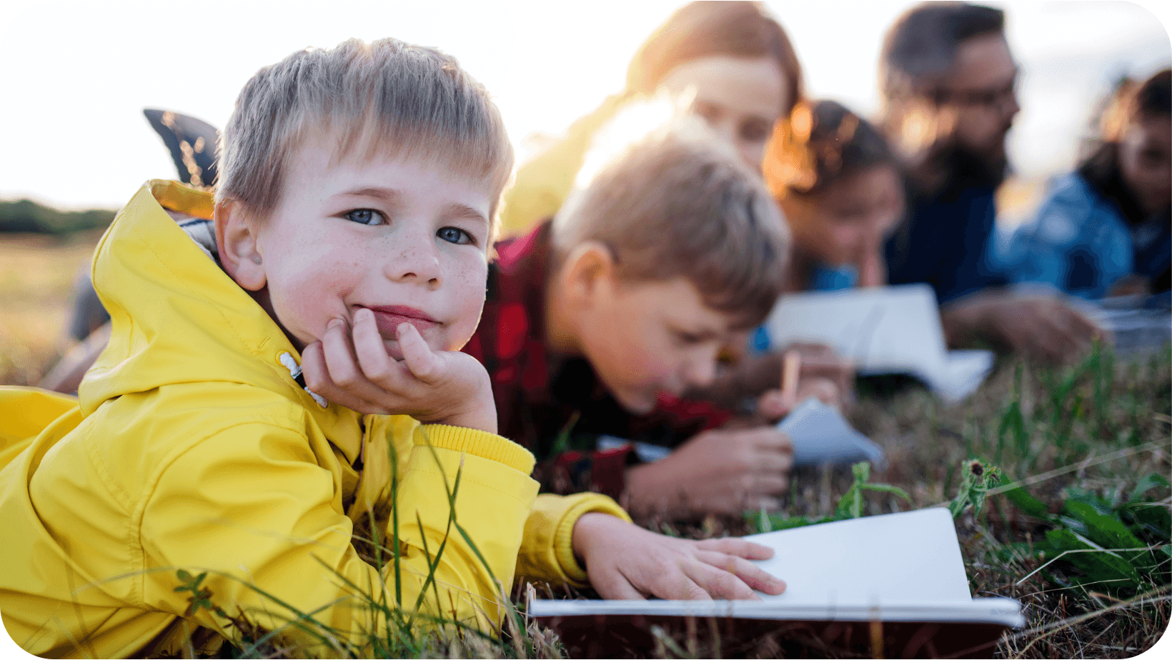 Young children reading books lying on the grass in a field with their parents