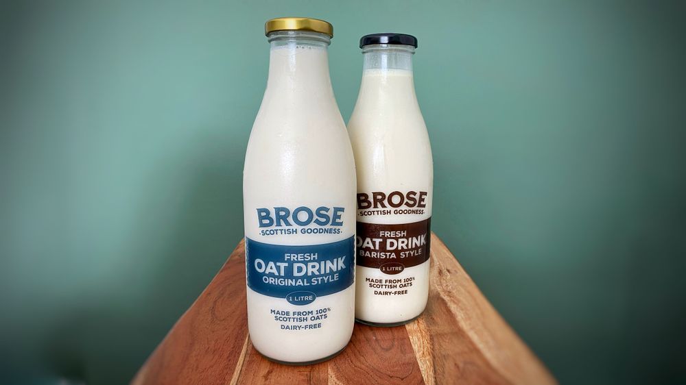 Two glass bottles of Brose oat drink on a wooden table with a green background