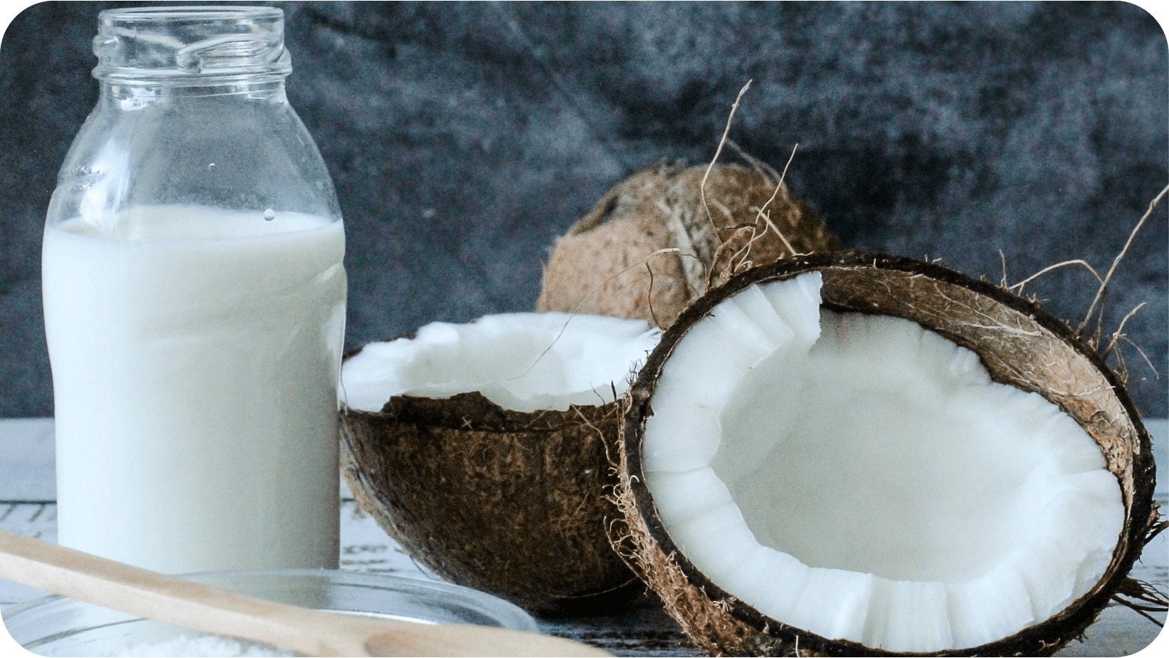 Coconut halves next to a glass bottle of milk