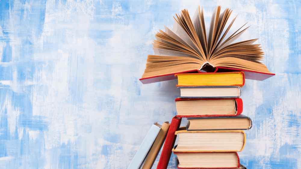 Stack of colourful hardback books and an open book at the top of the stack, on a blue background