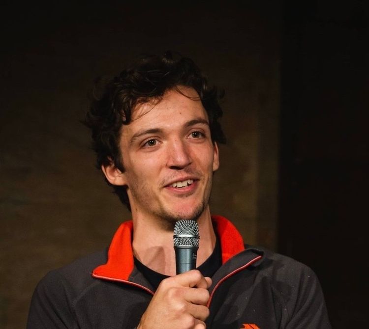 Rory Cockshaw smiling and holding a microphone on stage in front of a crowd