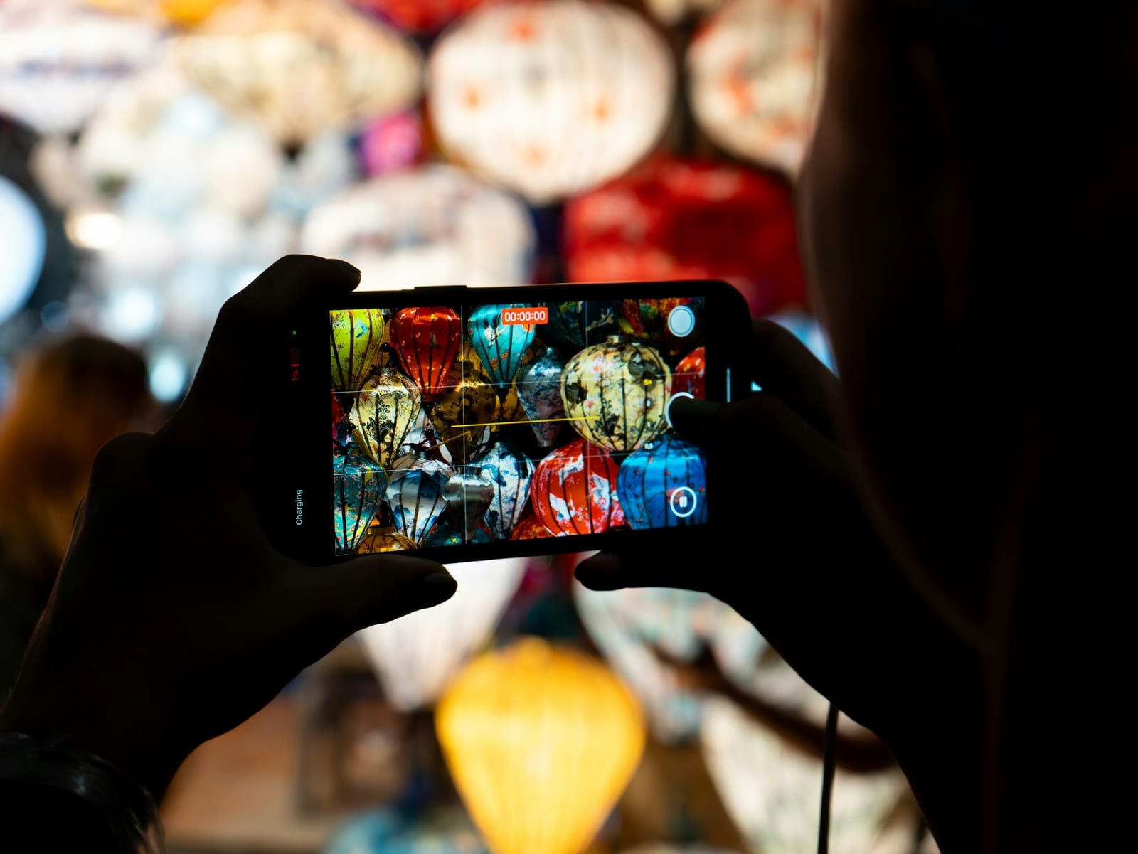 Iemand fotografeert gekleurde lampionnen met een telefoon