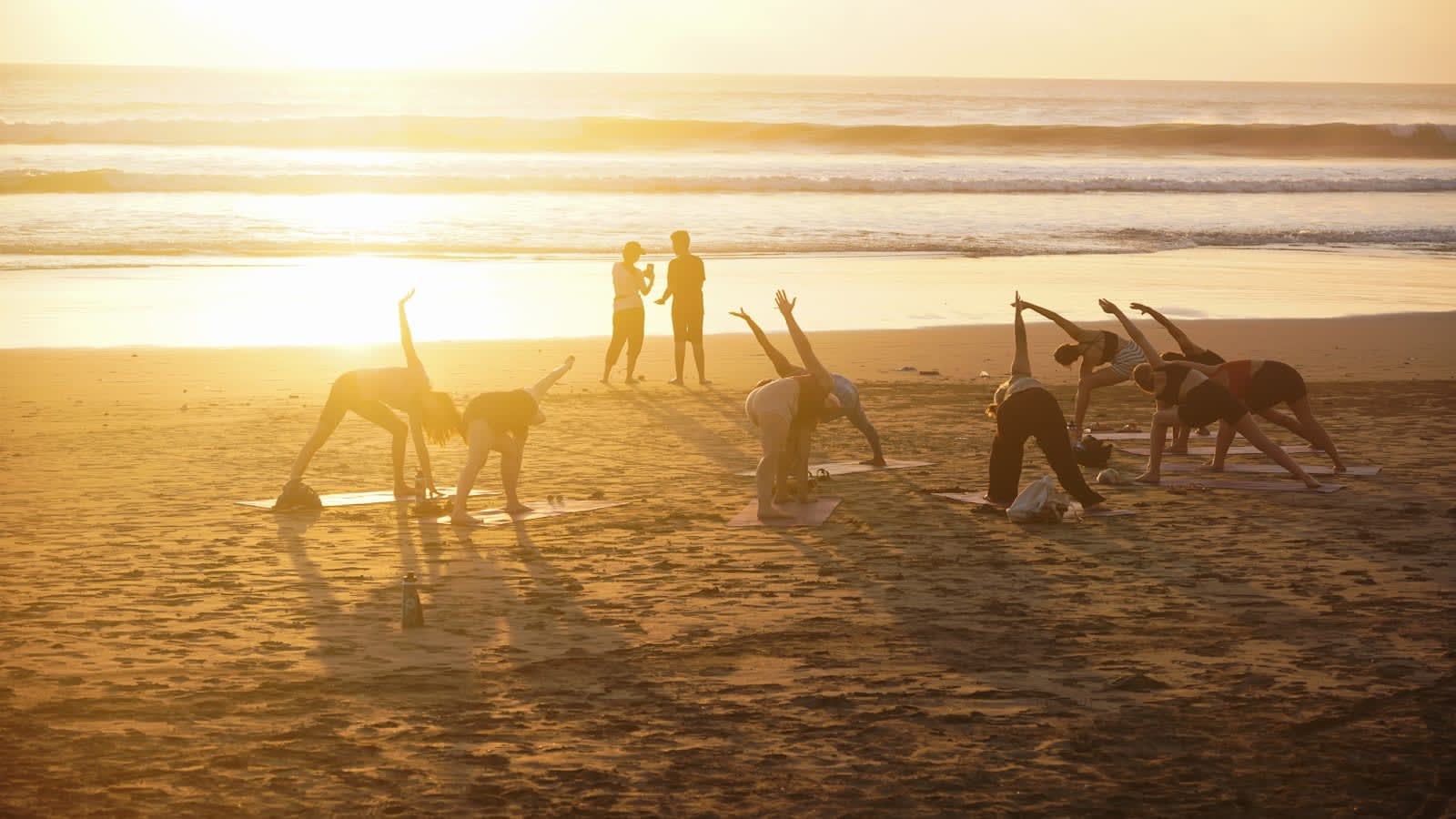 Groep die samen yoga doet op het strand bij zonsondergang