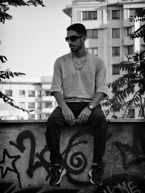 Model in a black graphic tee leaning against a graffiti covered wall