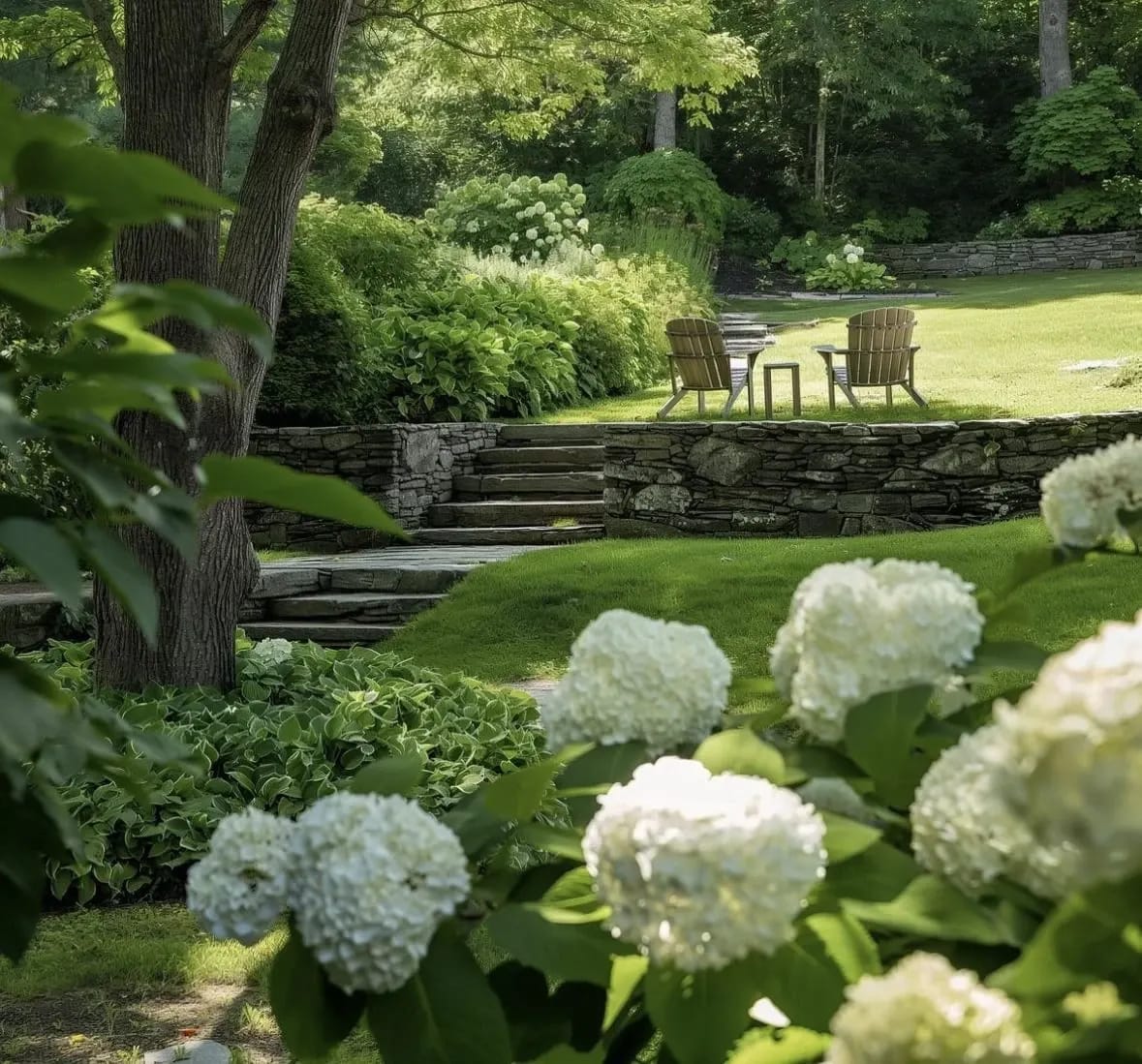 Jardin ombragé avec hortensias blancs, muret en pierre sèche et coin détente