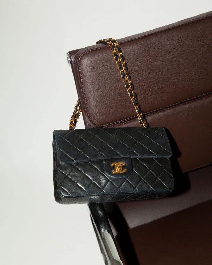 Sac de luxe en cuir box noir avec boîte d'origine et dustbag, posé sur une table en chêne huilé