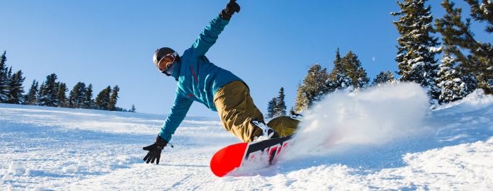 Snowboardeur descendant une piste enneigée - Vacances Bleues