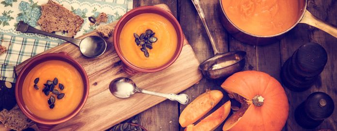 Bols de velouté de potiron présentés sur une planche en bois avec des ingrédients autour - Vacances Bleues