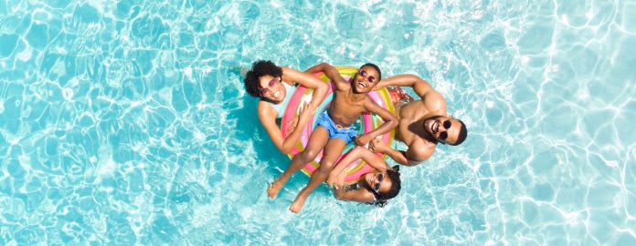 Une famille souriante avec deux enfants s'amuse dans l'eau d'une piscine claire, réunie autour d'une grande bouée colorée - Vacances Bleues