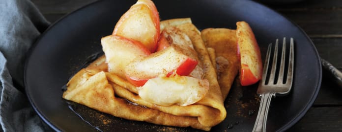 Assiette de crêpes garnies de pommes caramélisées et saupoudrées de cannelle, servie avec une fourchette vintage.