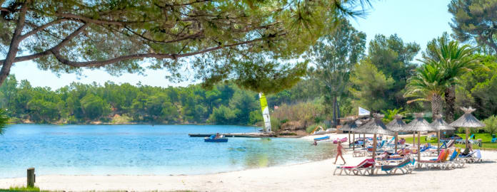 Plage privée avec transats et parasols en paille face à la lagune sous un ciel bleu - Club*** Plein Sud - Hyères les palmiers