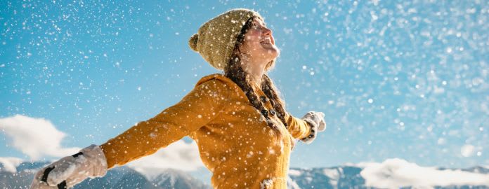 Femme souriante profitant d'une neige abondante en montagne, vêtue d'un manteau jaune et d'un bonnet.