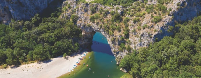 Vue aérienne du Pont d'Arc avec des canoës sur la rive et dans l'eau