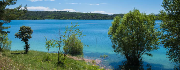Vue du lac de Montpezat entouré de végétation sous un ciel bleu - Club*** Château Laval - Gréoux les Bains