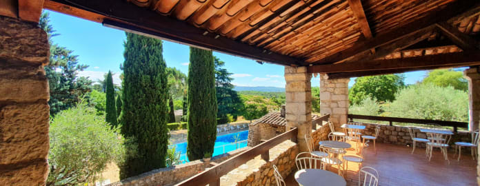 Vue de la piscine depuis la terrasse extérieure couverte avec en arrière plan des arbres à perte de vue sous un ciel bleu- Résidence 3* Lou castel - Ardèche