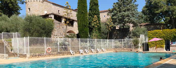 Vue de la piscine extérieure avec des personnes se baignant et en arrière plan le château en pierre - Résidence 3* Lou Castel - Ardèche